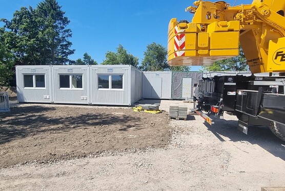Container und ein gelbes Fahrzeug Am 12. Mai hat die Lieferung und Montage der Wohncontainer begonnen. Die letzten Container werden am Mittwoch (14. Mai) erwartet. Für die abschließenden Innenarbeiten benötigt die Lieferfirma etwa zwei Tage. In der folgenden Woche können die Anschlussarbeiten fortgesetzt werden. Für die Zeit der Anlieferungen ist eine Ampelanlage eingerichtet worden, die abends nicht mehr aktiv ist. Für etwaige Behinderungen während der Montage bittet die Gemeindeverwaltung um Verständnis.