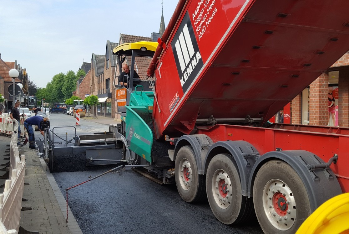 Der Asphaltfertiger schiebt sich langsam über die Straße und verteilt dabei gleichmäßig den Asphalt der Deckschicht. Abstandshalter gewährleisten die passgenaue Einbringung des Asphalts.  (Bild: Gemeinde Senden)