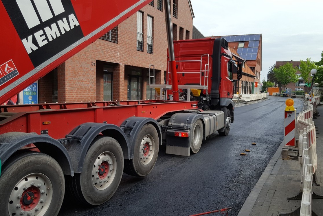 Der Kipper mit dem Asphalt wird vom Asphaltfertiger gleichmäßig vorangeschoben. Rechts zu sehen: die Schieberkappen, die nach Einbringen der Deckschicht bündig mit der Straßenoberfläche sein werden. (Bild: Gemeinde Senden)