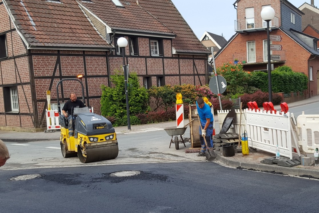 Die kleine Walze verdichtet den Asphalt an den Übergängen zum "alten" Straßenbereich. Überschüssiger Asphalt an den Kanten wird entfernt. (Bild: Gemeinde Senden)